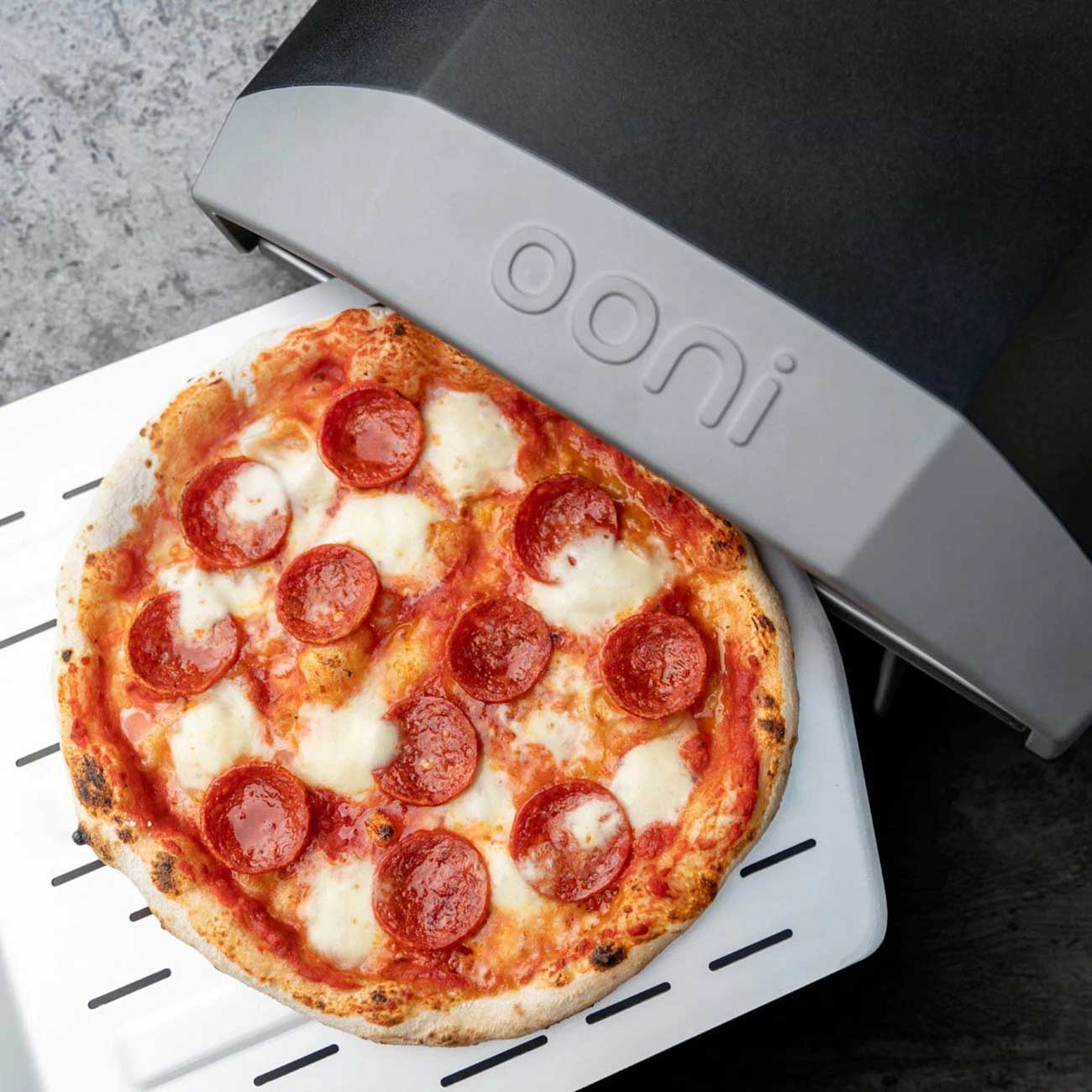 Person Placing Pizza Inside an Ooni Koda 12 Pizza Oven