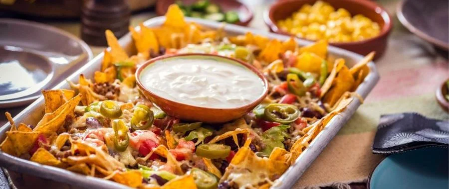 A tray of loaded nachos with a bowl of white queso in the center