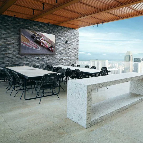A stone patio with a stone counter, tables, chairs and an outdoor TV displaying car racing.