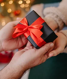 person handing someone a black gift box wrapped in a red bow