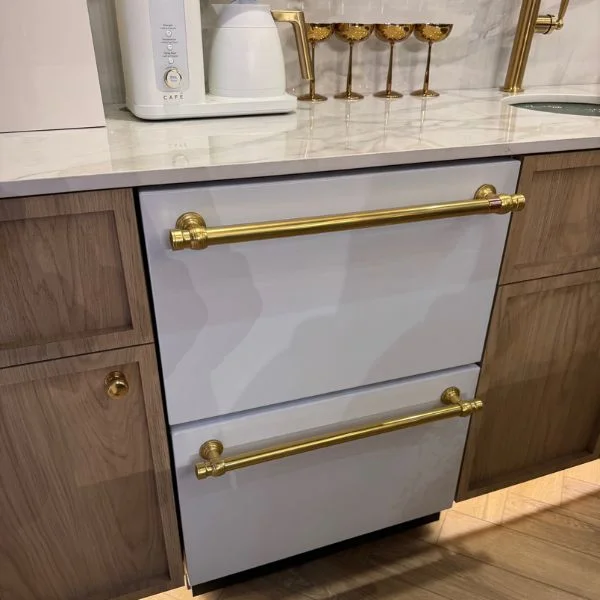 White Cafe double dish drawer with brass handles installed between light wood cabinets
