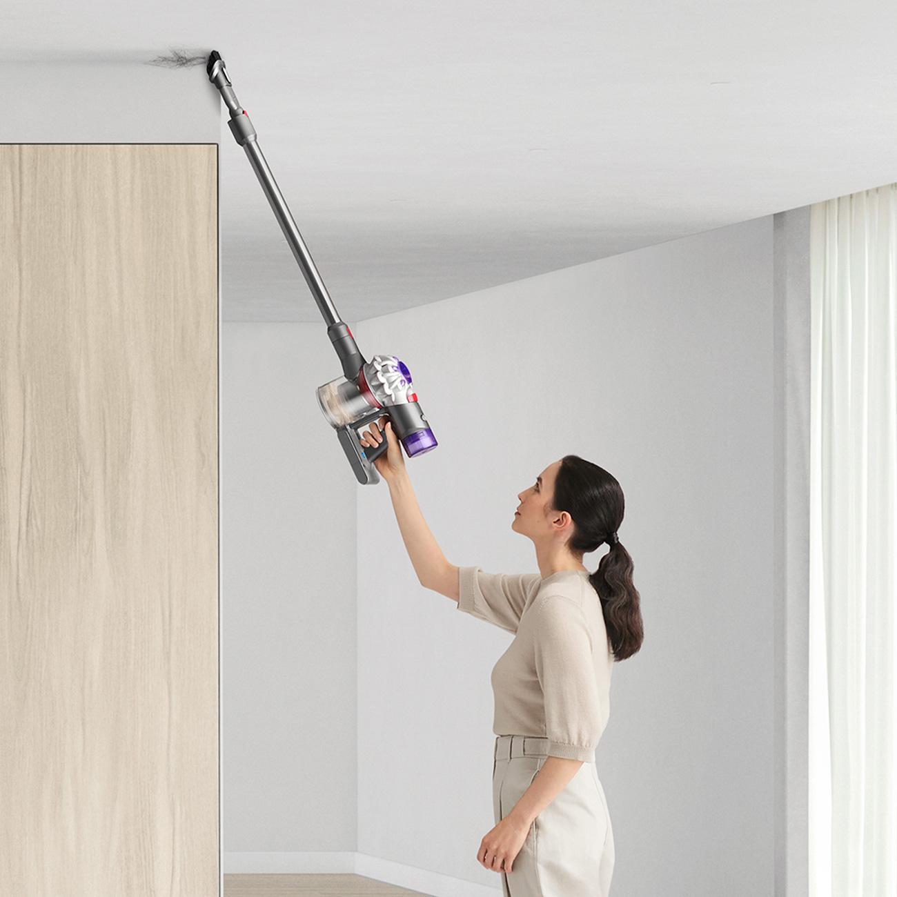 Woman with Beige Top Cleaning a Ceiling with a Dyson V8 Cordless Stick Vacuum
