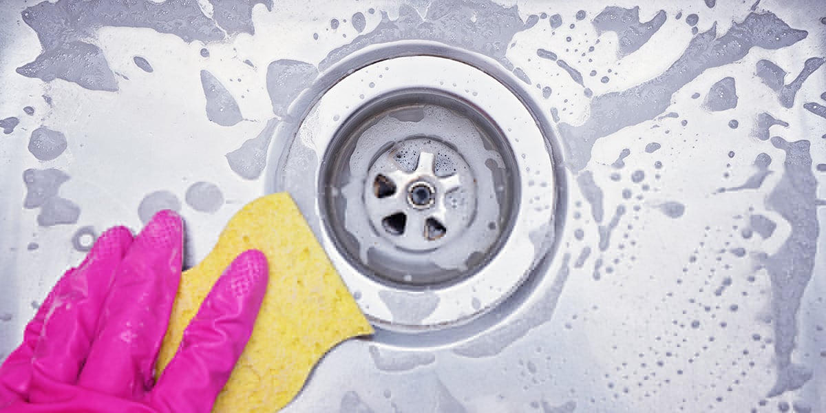 A zoomed-in photo of a sink's bowl with soapy water and a pink gloved hand scrubbing the basin