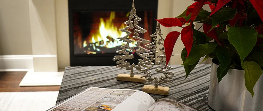 A book sitting on a coffee table with flowers and decorative Christmas trees in front of a fireplace