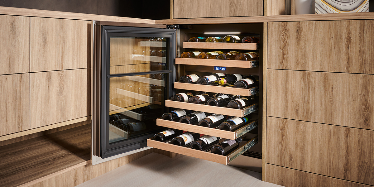 A set of wooden kitchen cabinets with a built-in wine refrigerator and the shelves of wine bottles are pulled out