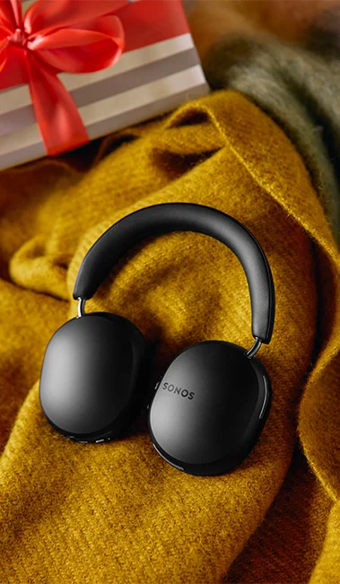 Close up on the Sonos Ace Headphones on a mustard yellow blanket with a wrapped gift in the top left hand corner