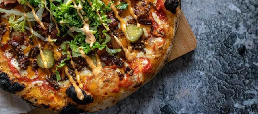 A pizza covered in ground meat, pickles, cheese, lettuce and burger sauce