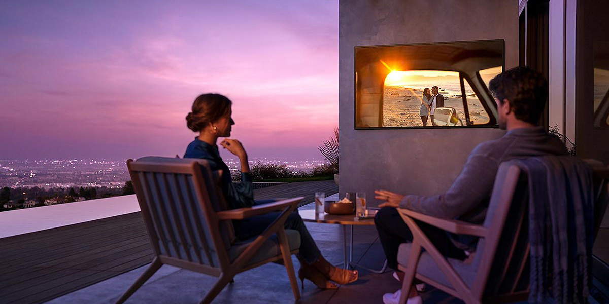 A couple sitting on their building's balcony, watching their outdoor TV