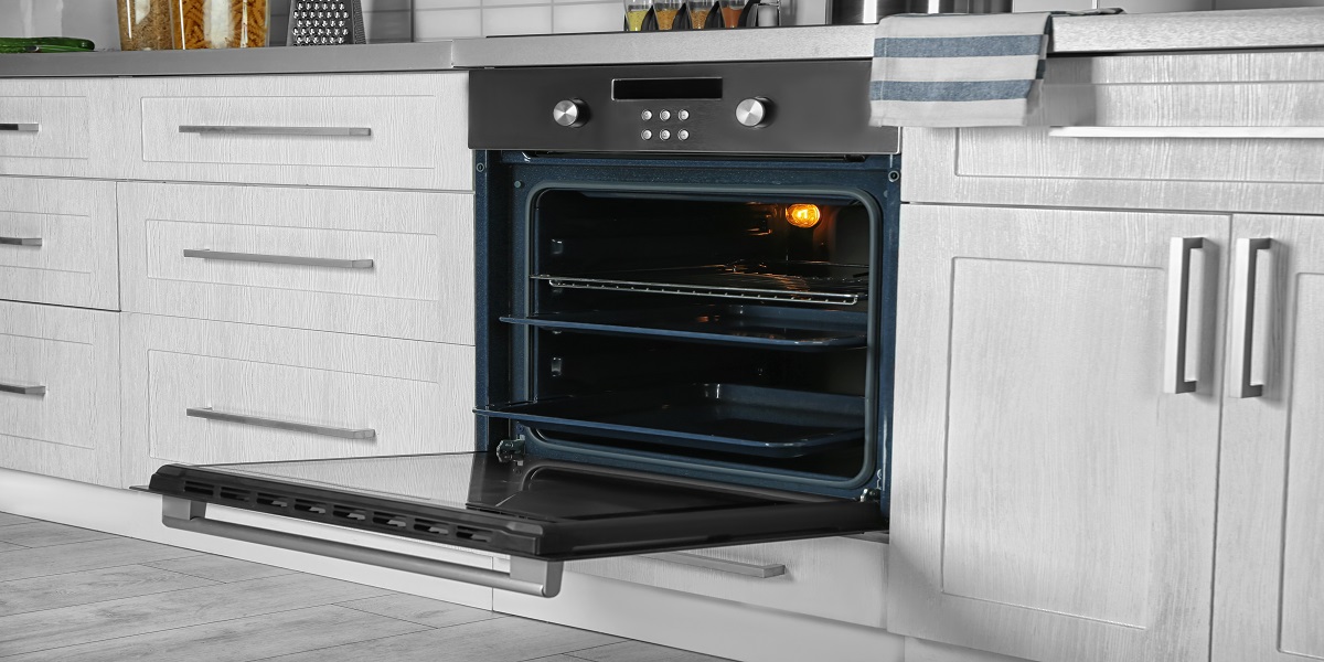 Open electric wall oven installed in white cabinets