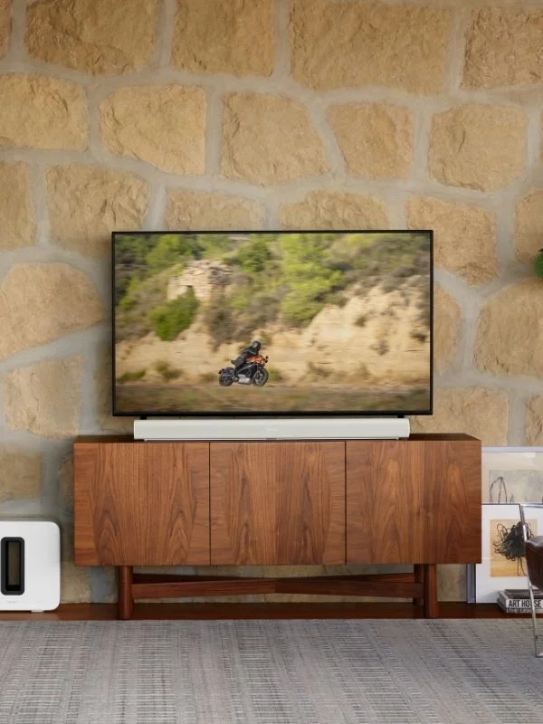 Sonos soundbar stop a tv entertainment stand with a tv showcasing someone on a motorcycle all in a modern living room with exposed stone on the wall