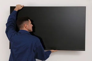 A man in a blue shirt hanging a new television on the wall