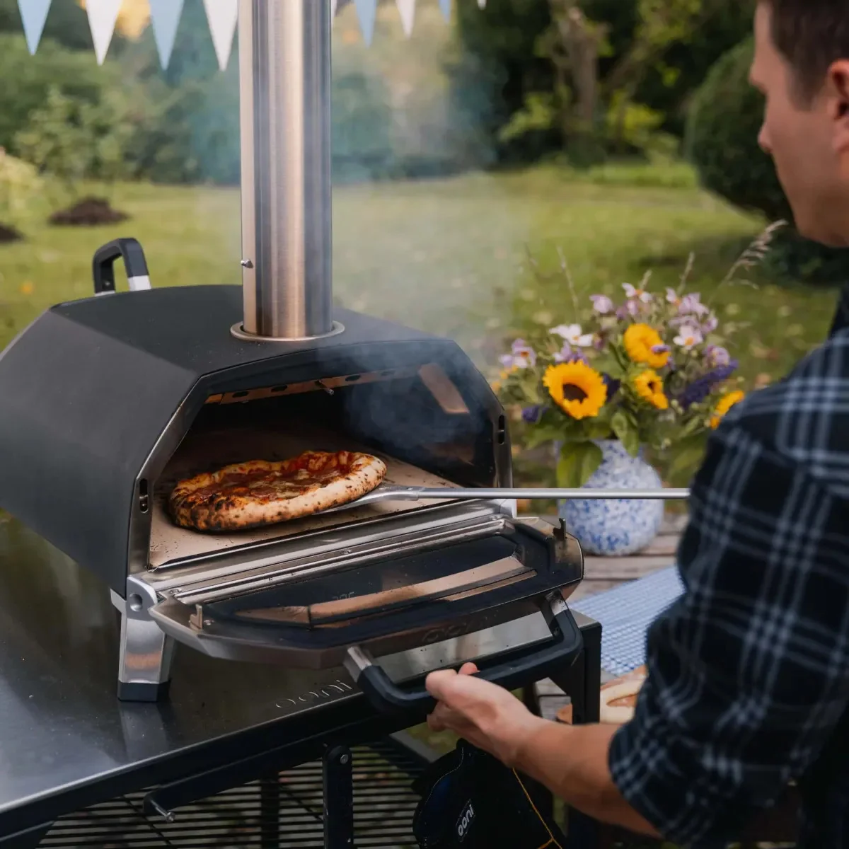 A man removing a cooked pizza from his Ooni Karu 16 pizza oven using a peel.
