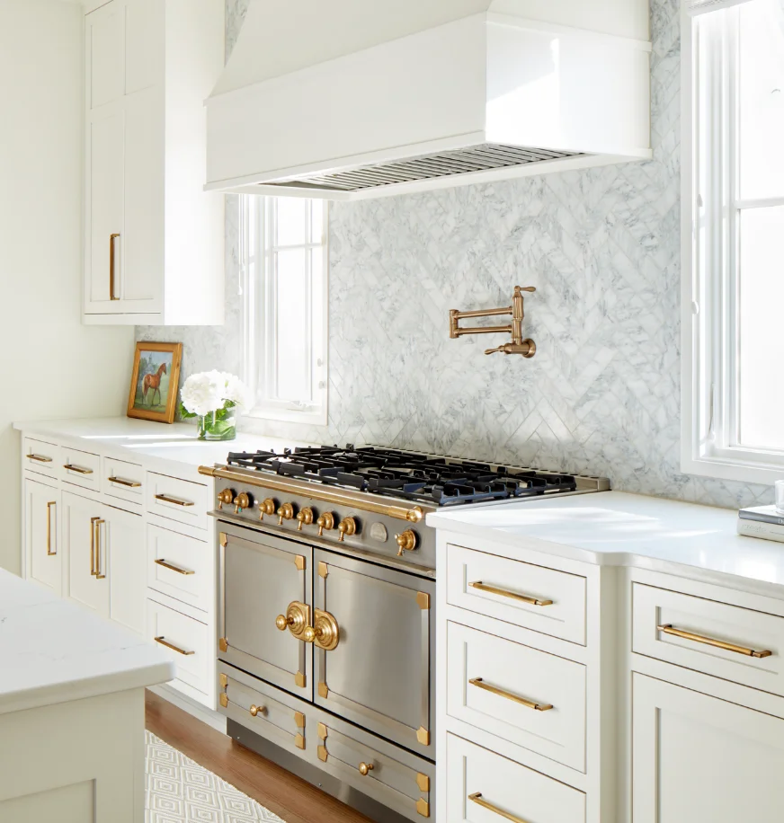 La Cornue range in a white kitchen with marble herringbone backsplash and a brass pot filler