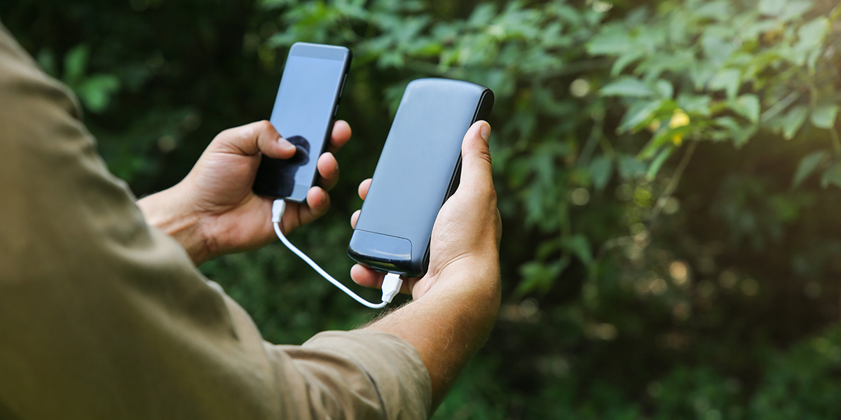 A man in a green shirt holding both a portable charger and a cell phone. the charger is charging the phone