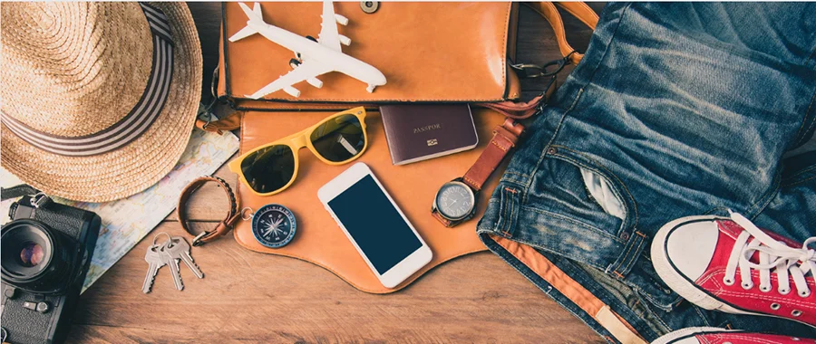 A collection of travel gear inclusing a camera, a hat, sunglasses, a smartphone, a watch, clothing and more