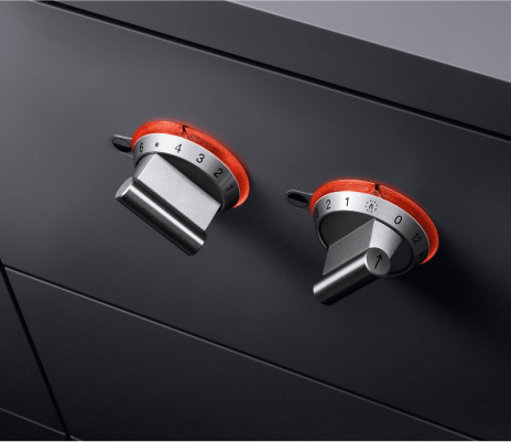 Close-up of two black cabinet knobs with red handles, showcasing a Gaggenau appliance accessory option