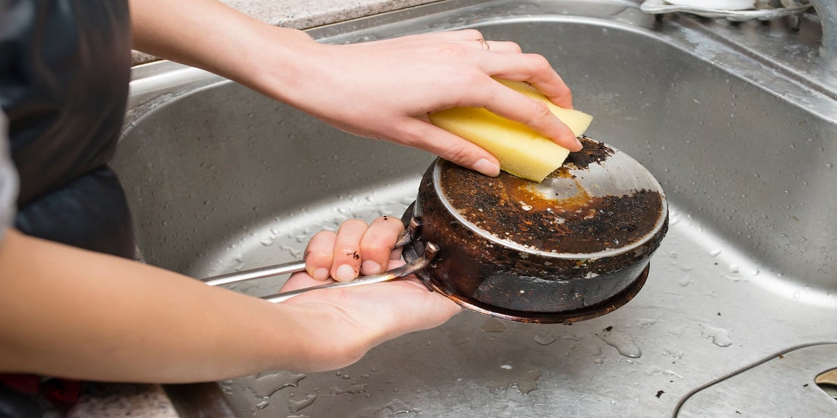 Person removing burnt food from pan with a sponge