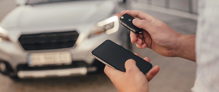 Someone holding a remote start key fob while standing in front of their car