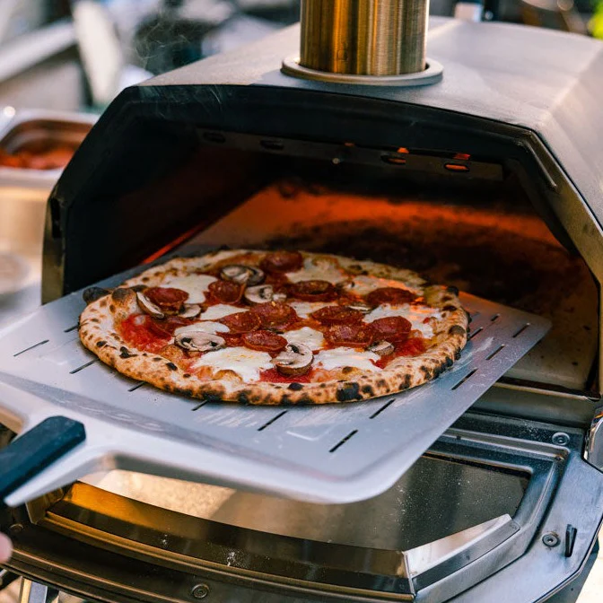 A cooked pepperoni pizza getting taken out of an Ooni Karu 16 pizza oven