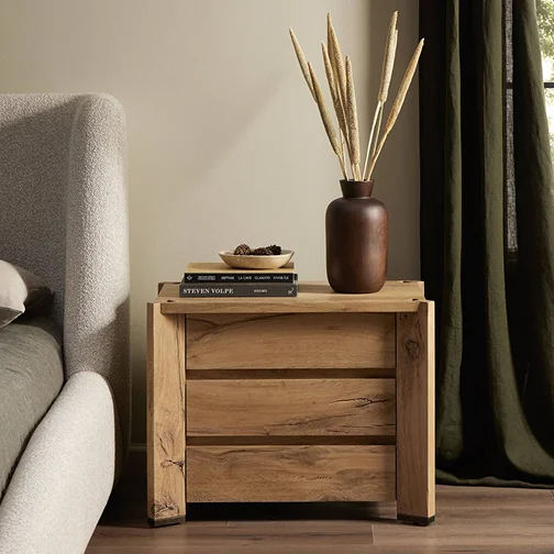 A wooden nightstand featuring a decorative vase on top, set in a cozy bedroom environment