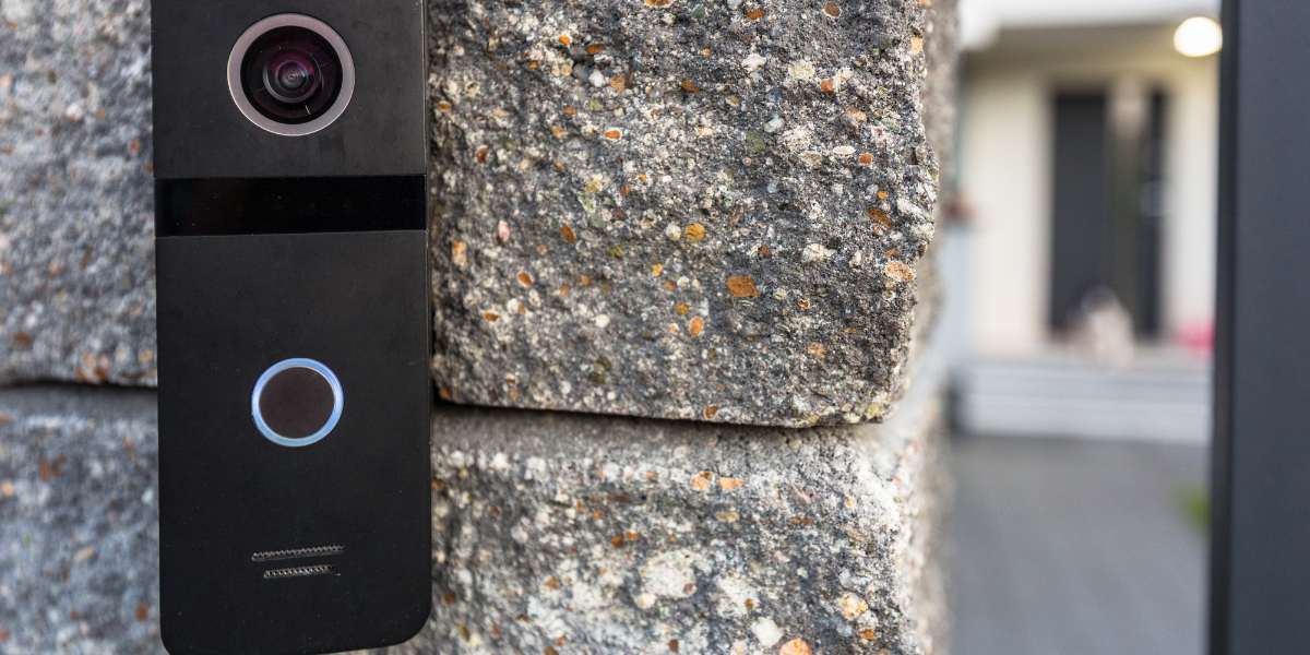 A black video doorbell sitting against a stone home exterior