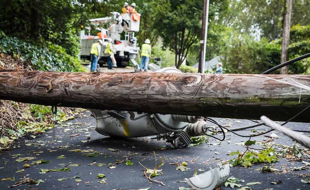 Power lien and pole blocking street with electric crew in the background