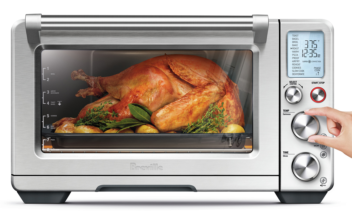 Person Adjusting Settings on a Breville The Smart Oven Pro Air Fryer with a Chicken Roasting Inside
