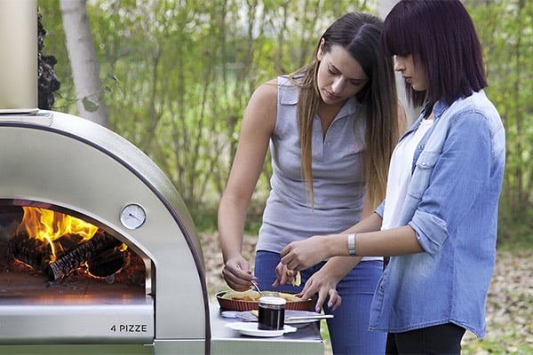 Two Women Finishing A Pizza Recipe Before Placing It In The Outdoor Pizza Oven