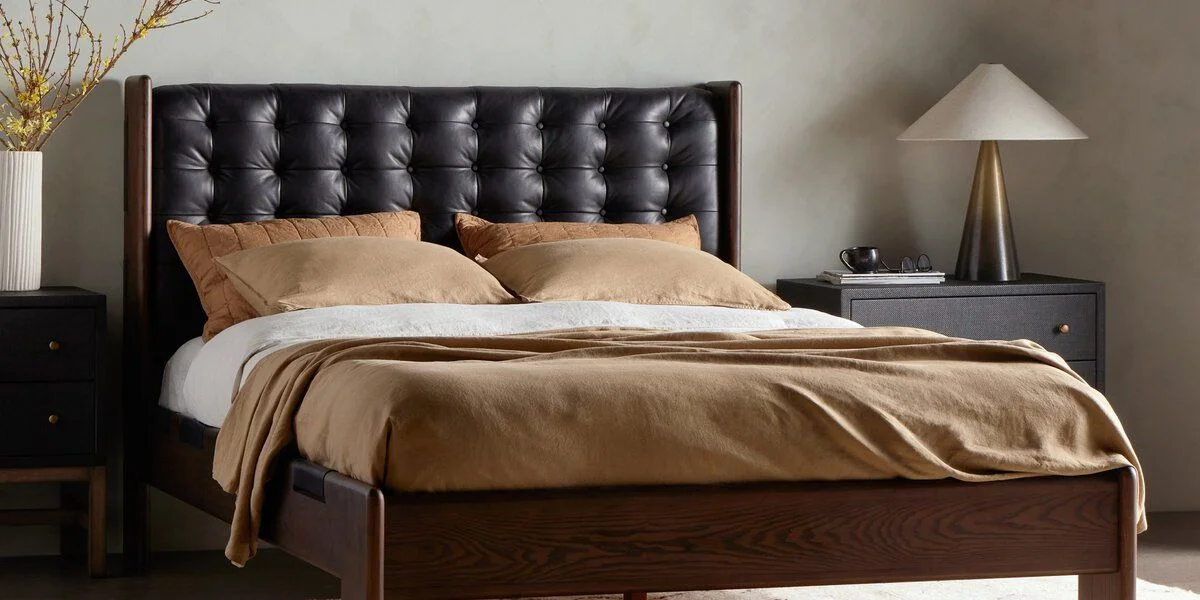 Bed with quilted leather headboard. Pillows and bedding in shades of tan and caramel top the bed, and there are dark wood nightstands on either side of the bed