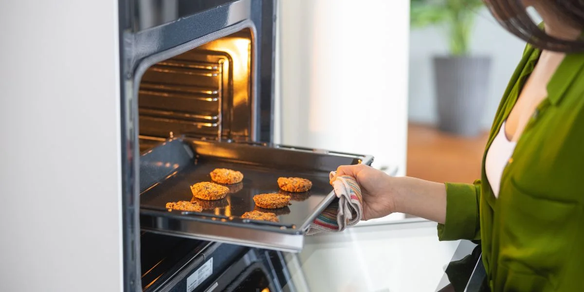 A woman placing a tray of chicken nuggets into a convection oven.