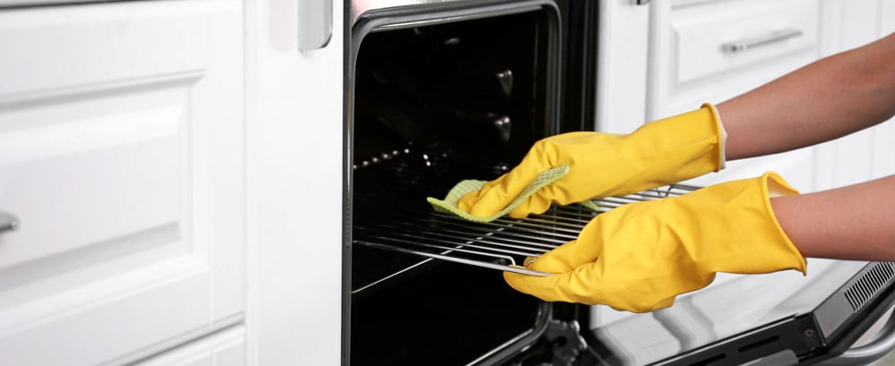 Cleaning oven in kitchen with yellow rubber gloves