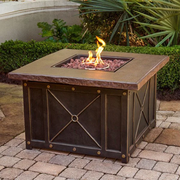 A brown fire pit sitting on a stone patio with flames coming out of it.