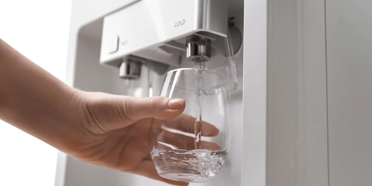 Person filling glass of water from refrigerator water dispenser