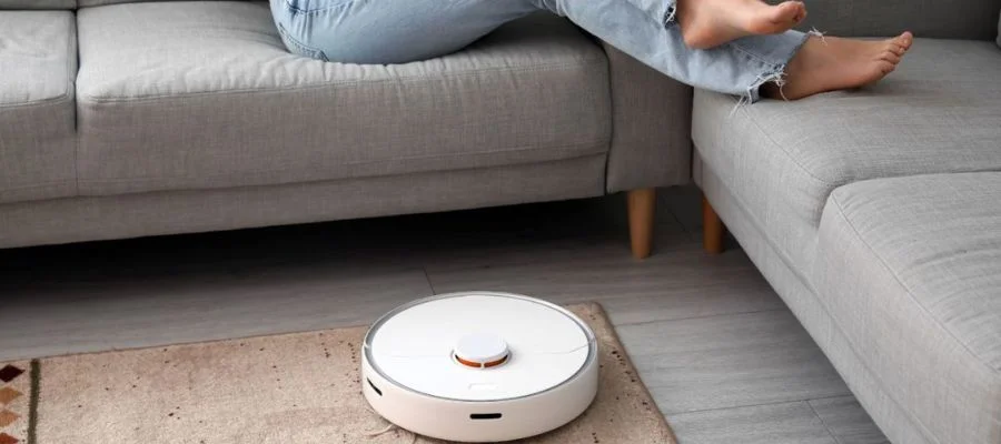 A vacuum robot roams the living room while a person lounges on the couch.