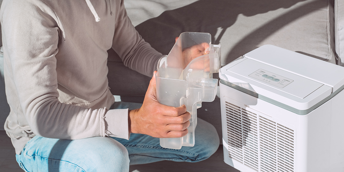 A man crouched down next to a white humidifier holding the water tank