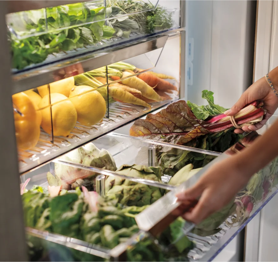 Close-up of a person opening a Sub-Zero refrigerator, showcasing a detailed vegetable and fruit drawer