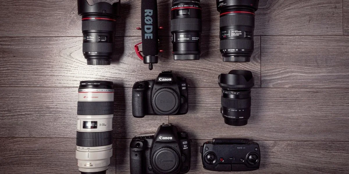 A collection of Canon cameras and lenses, along with a RODE microphone, on a wooden surface.