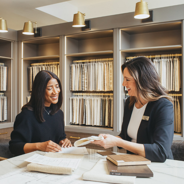 people sitting at a wooden table with swatches, mock up designs and books showcasing planning and designing a furniture space