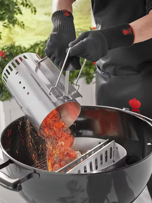 A person using a weber chimney fire starter to ignite a flame on a charcoal grill