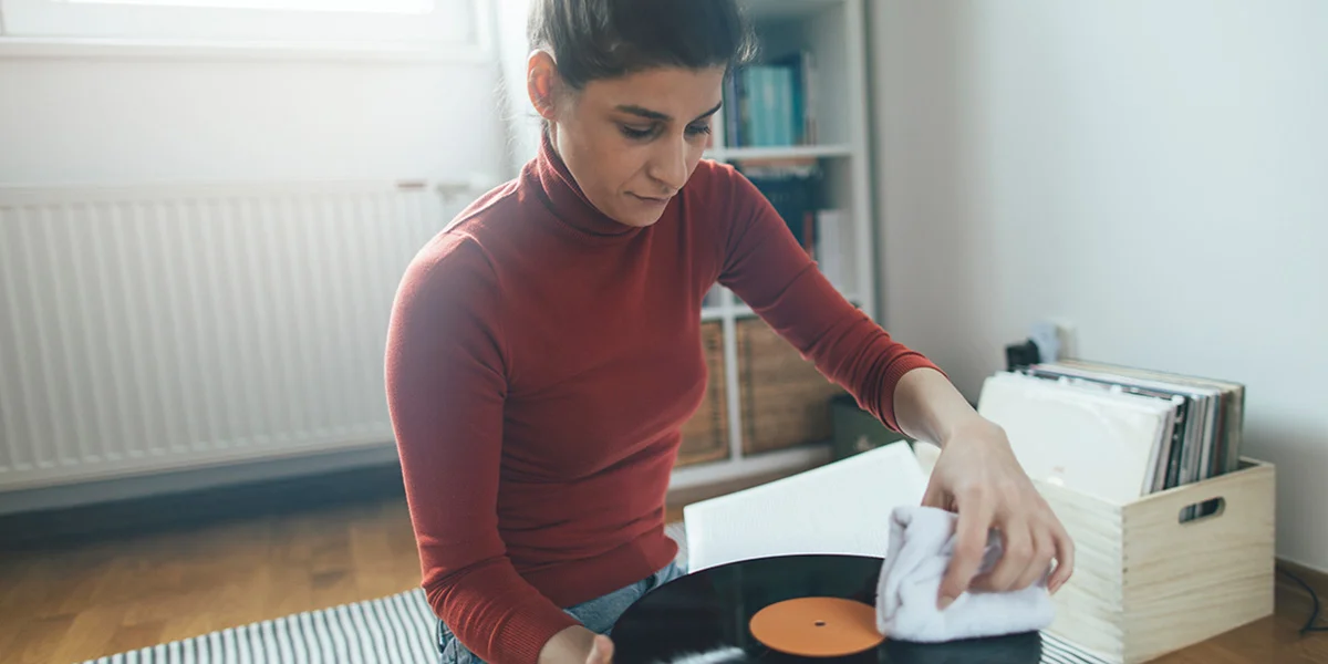 A young woman in a red turtleneck cleans her vinyls by hand with a microfiber cloth in her apartment