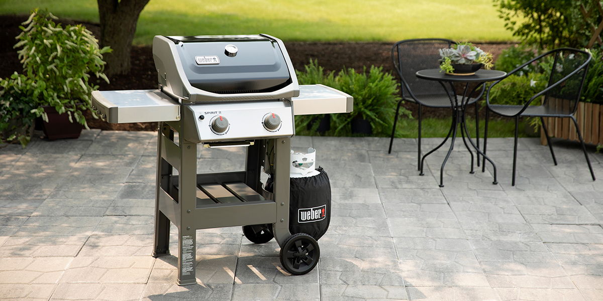 A black and stainless propane grill sitting on a grey stone patio