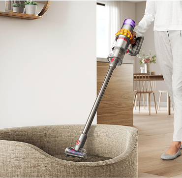 A person using a Dyson Stick Vacuum to clean a dog bed