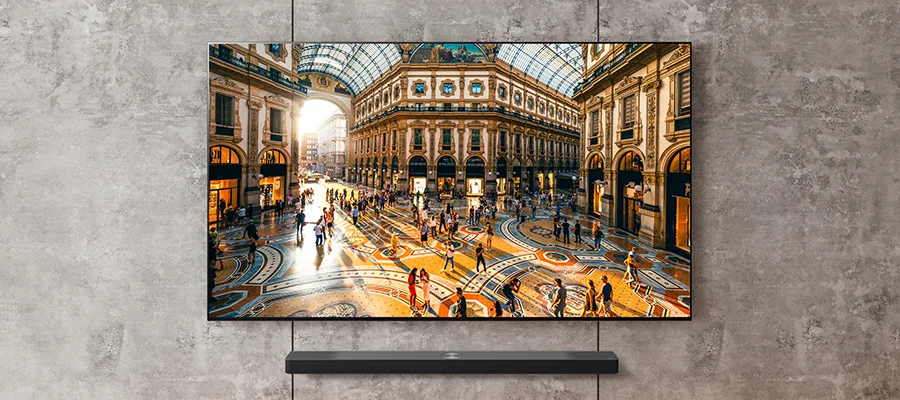 The LG S95TR soundbar mounted on a grey wall beneath a TV displaying the inside of a building with intricate architecture
