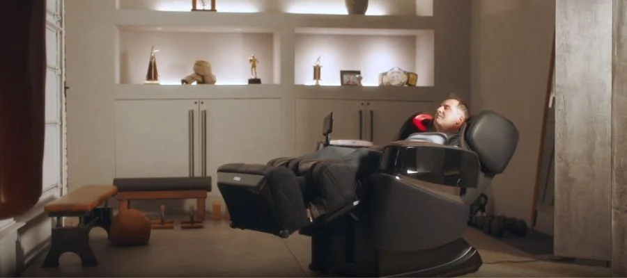 A man using his massage chair, leaning back into it in a room filled with trophies and champion belts