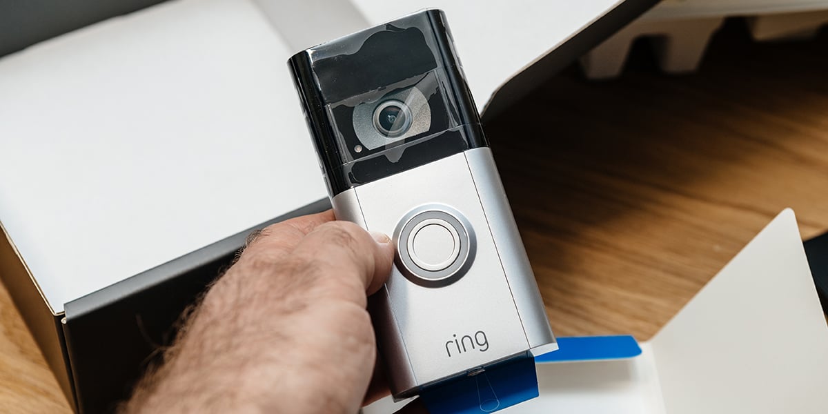 A hand holding a silver and black smart Ring doorbell fresh out of the manufacturer's box