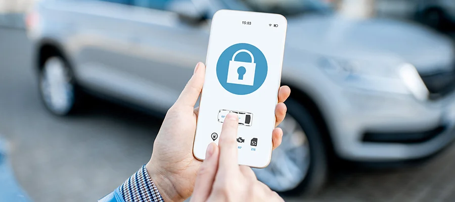 Someone standing outside of their silver car with the remote start app open to unlock their vehicle.