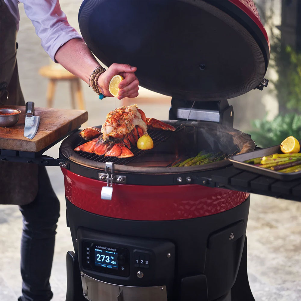 Person Juicing a Lemon Over Lobster Grilling on a Kamado Joe Charcoal Smoker and Grill