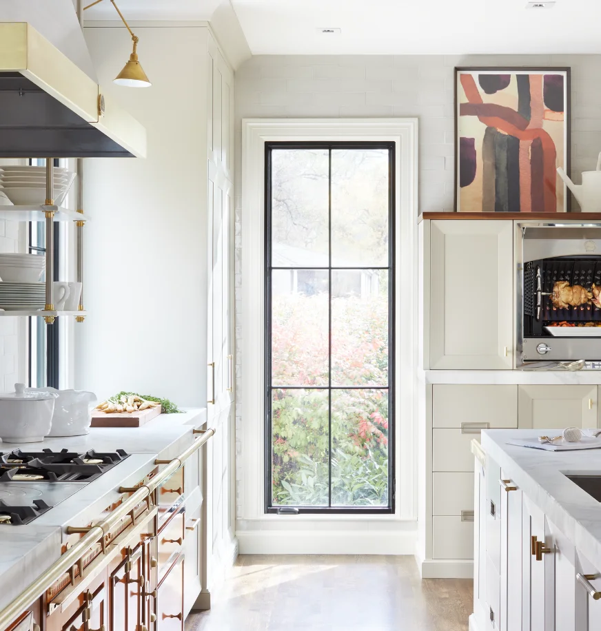 La Cornue range in a cream kitchen with a tall arched window and built-in rotisserie roasting a chicken