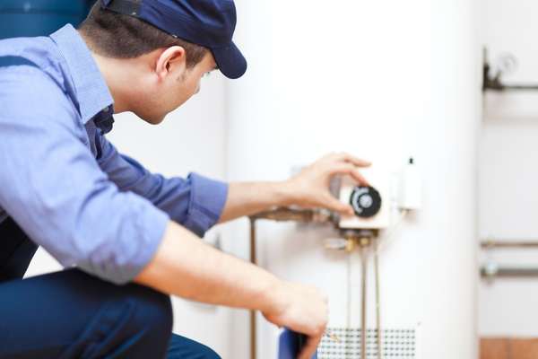 Workman in a blue hat adjusting dials on a tank water heater
