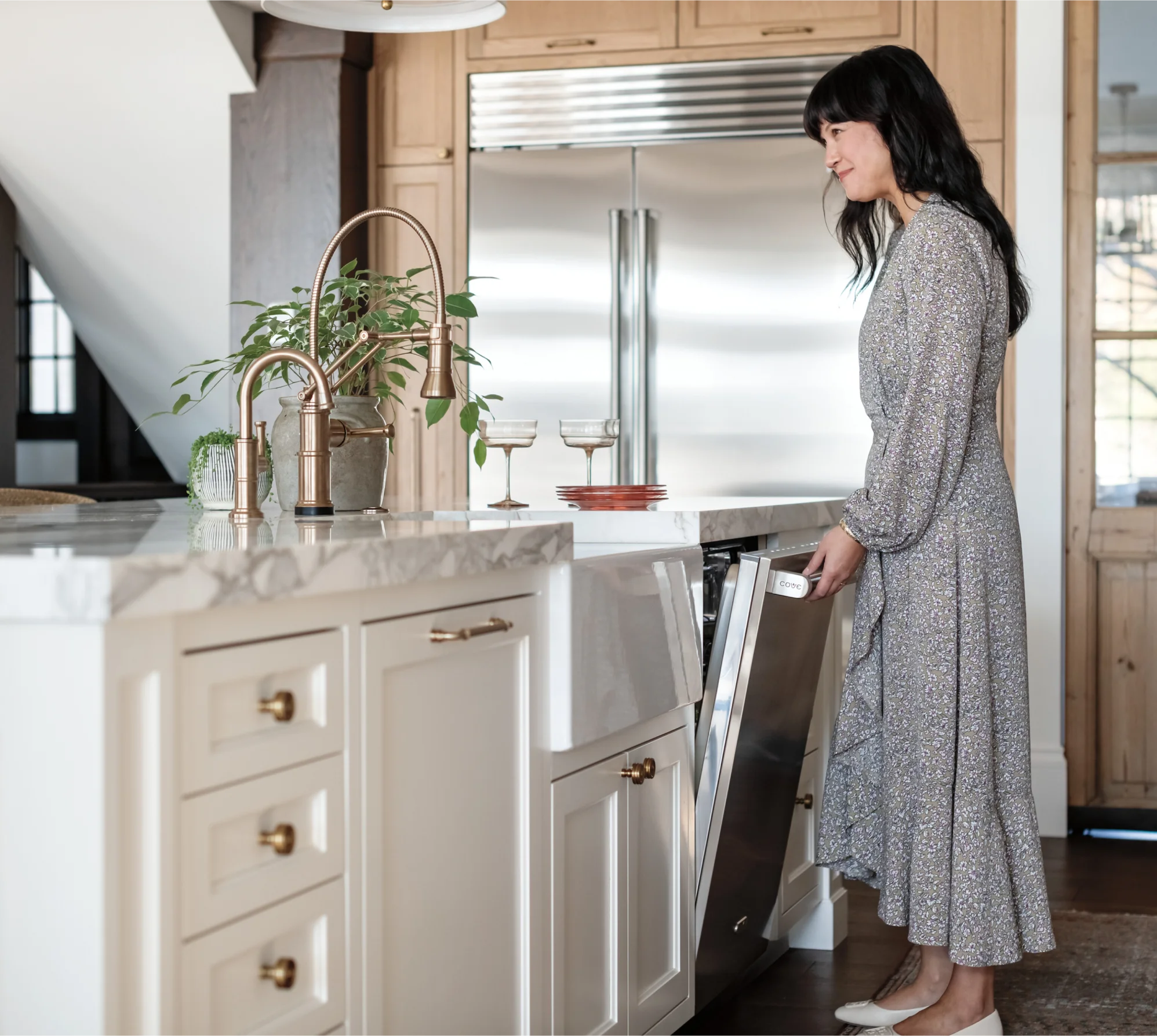 A woman in a dress stands in a modern kitchen, showcasing a Cove Built In Dishwasher